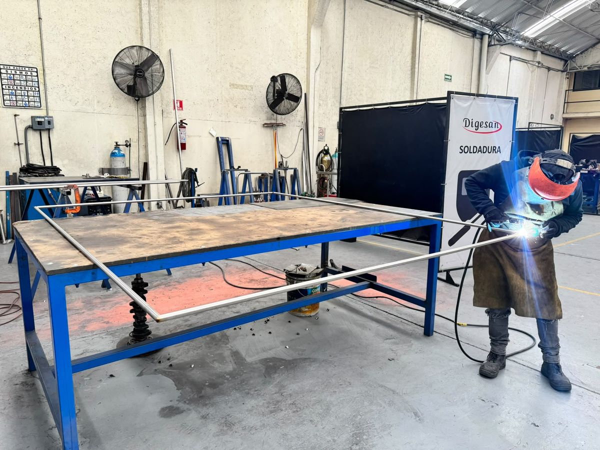 Soldador uniendo una estructura de tubo de acero inoxidable sobre mesa de trabajo
